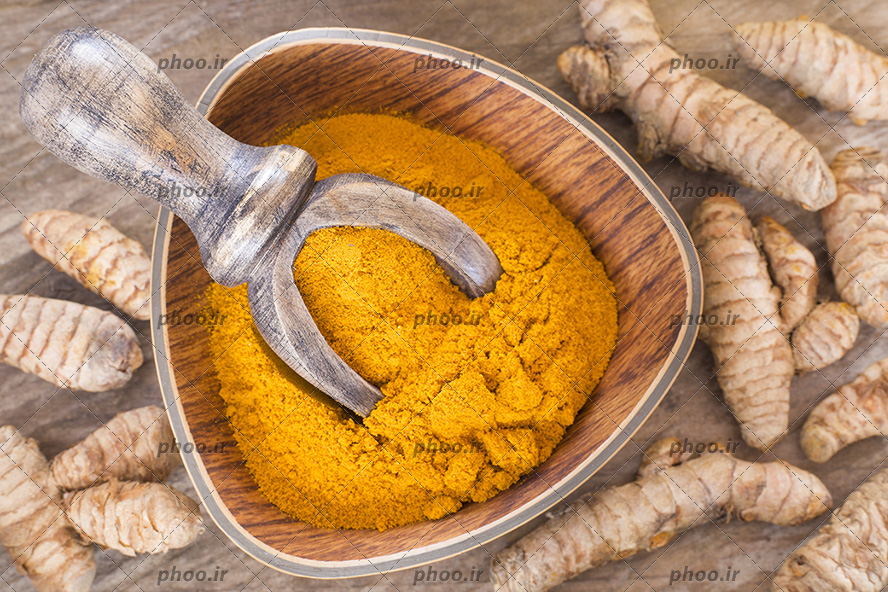 عکس زردچوبه روی زمین و پودر زردچوبه در کاسه چوبی از نمای بالا