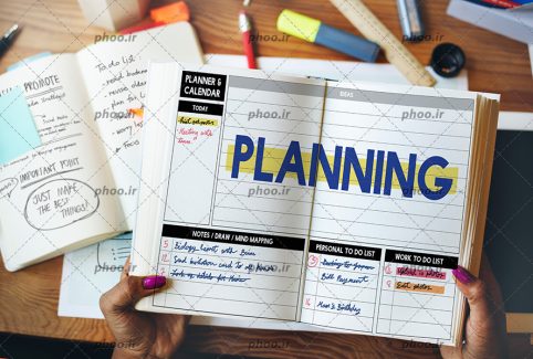 عکس کتاب در دست دختر با نوشته انگلیسی (planning) به معنی برنامه ریزی در کنار کتاب ها و لوازم دیگر روی میز چوبی