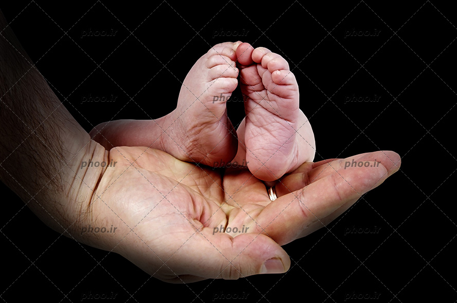 عکس با کیفیت پاهای کوچک نوزاد در دست پدر در پس زمینه مشکی