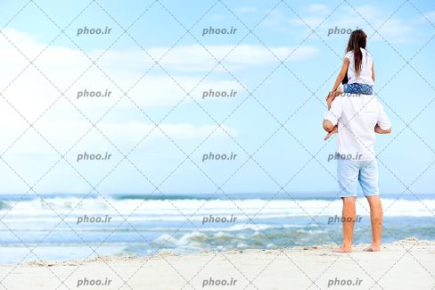 عکس با کیفیت دختر بر روی دوش پدر ایستاده در کنار دریا در حال تماشا کردن آن