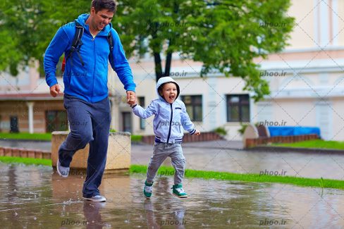عکس با کیفیت پدر و پسر شاد در حال بازی زیر باران در شهر