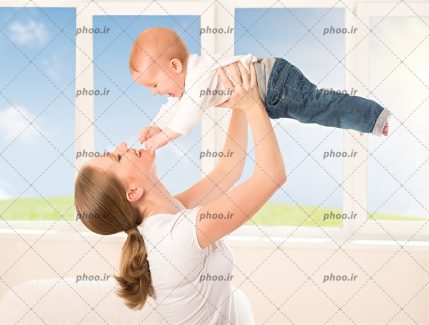 عکس با کیفیت مادر جوان شاد در حال بازی با کودک در کنار پنجره