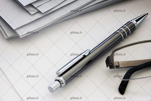 عکس خودکار و عینک و تعدادی برگه روی میز