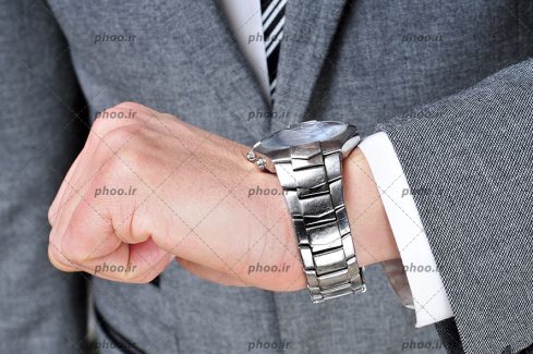 عکس یک آقا با کت طوسی در حال نگاه کردن به ساعت