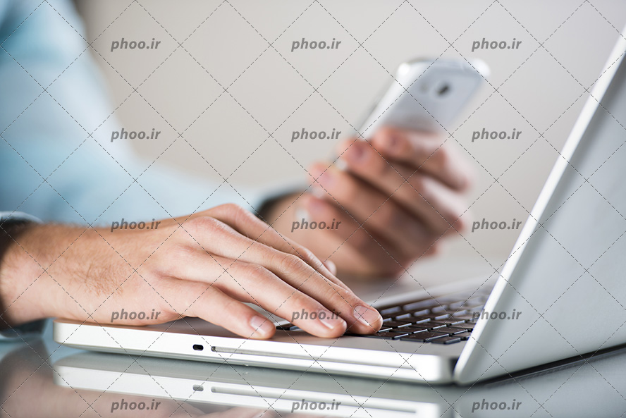 عکس مرد پشت میز و کار کردن همزمان با گوشی و لپ تاپ