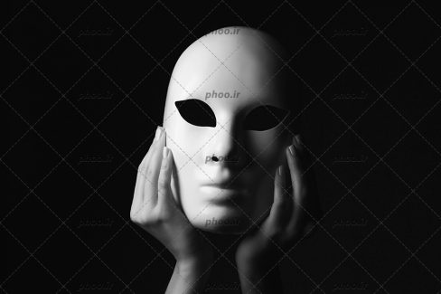 عکس دست هایی که ماسک سفید را نگه داشته اند در پس زمینه سیاه