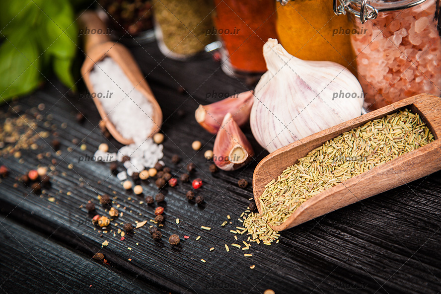 عکس ادویه هایی در قاشق های چوبی و روی زمین در پس زمینه چوب مشکی