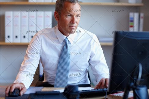 عکس یک مرد با پیرهن سفید و کراوات آبی در محل کار جلوی سیستم