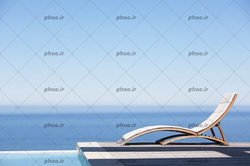عکس صندلی کرمی آفتابگیر در کنار دریا و آسمان آبی
