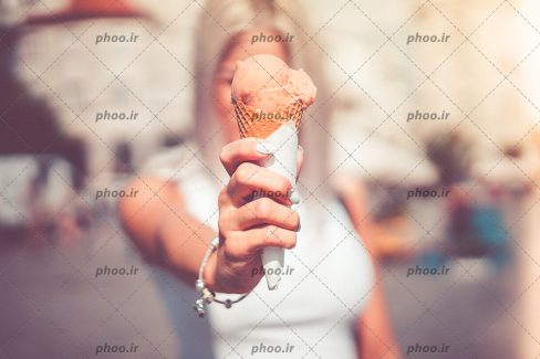 عکس بستنی قیفی صورتی در دست یک دختر با زمینه مات