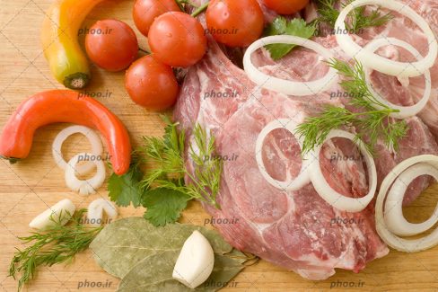 عکس گوشت خام با پیاز ها و سبزیجات روی زمینه چوبی