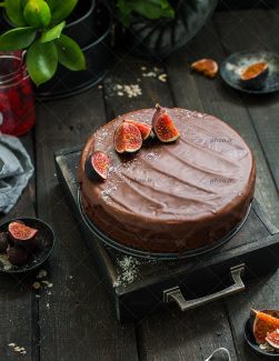 عکس کیک شکلاتی با تاپینگ انجیر روی میز چوبی و گل ها