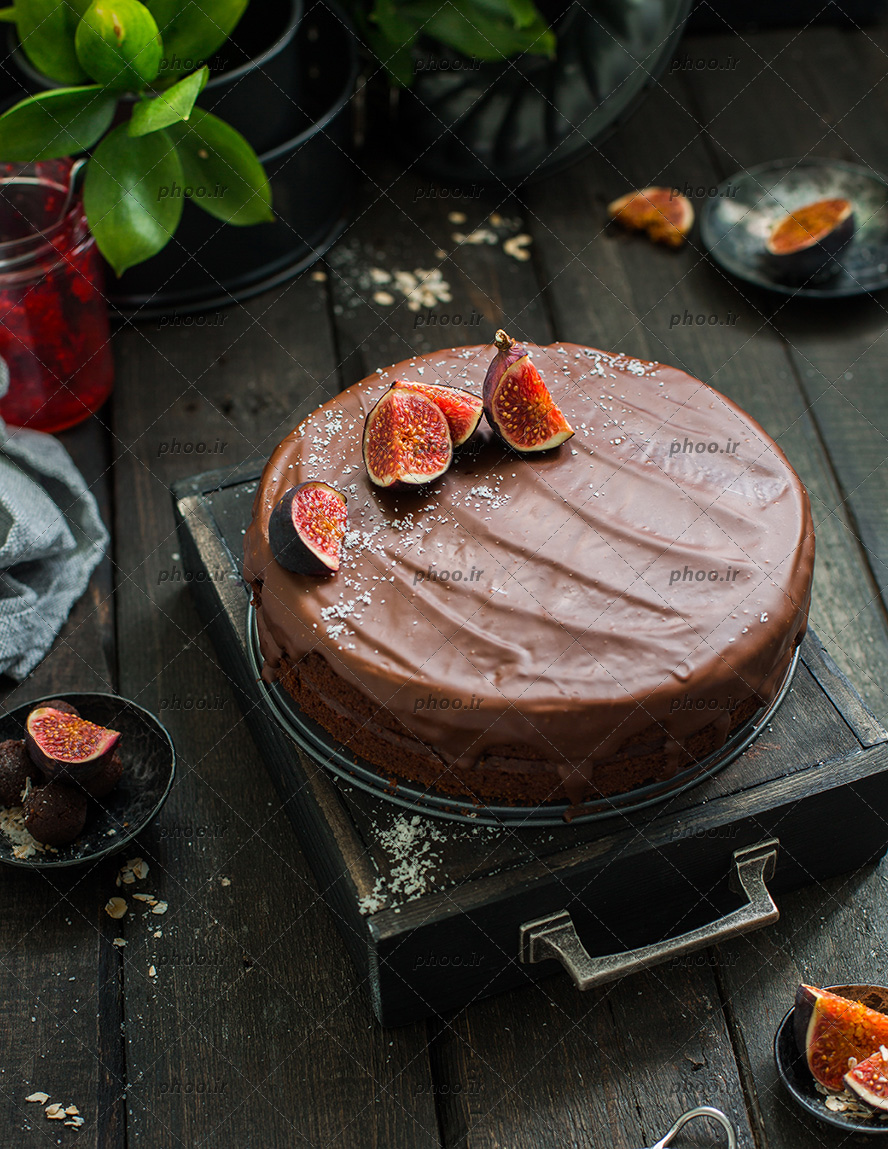 عکس کیک شکلاتی با تاپینگ انجیر روی میز چوبی و گل ها