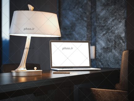 عکس لپ تاپ با صفحه نمایش حالی سفید در کنار چراغ مطالعه روی میز