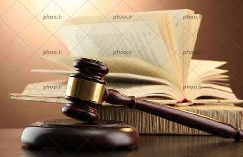 عکس با کیفیت چکش قاضی در کنار کتاب قانون روی میز در پس زمینه قهوه ای