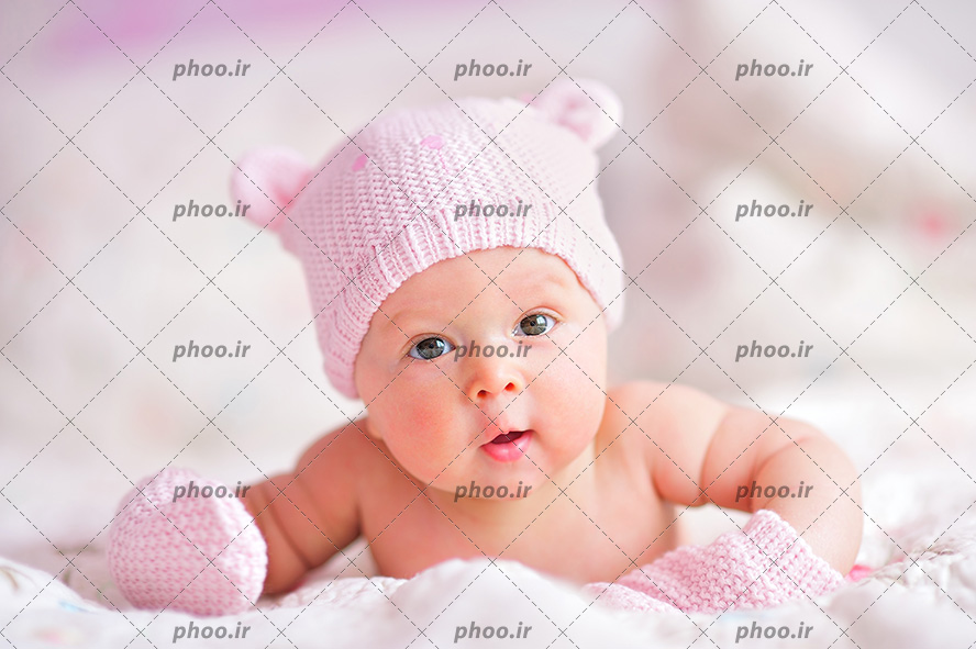 عکس با کیفیت نوزاد زیبا با دستکش و کلاه بافتنی صورتی در حال نگاه کردن به دوربین