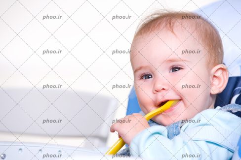 عکس با کیفیت کودک زیبا با لبخند و یک قاشق زرد در دهان