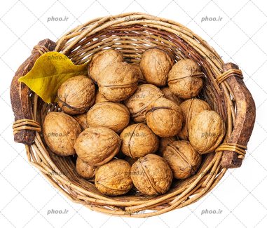 عکس سبد چوبی از گردو های سالم و یک برگ زرد از نمای بالا در پس زمینه سفید
