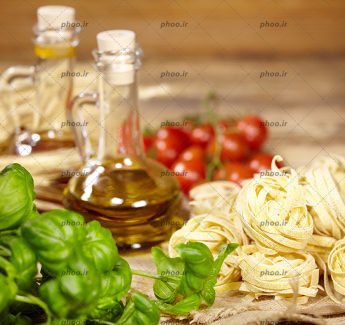 عکس ماکارونی های پیچ پیچی خانگی خام در کنار گوجه فرنگی و بطری های شیشه ای روغن روی میز چوبی