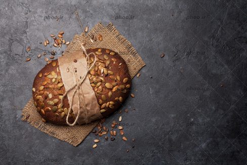 عکس نان گرد چاودار با تزئین مغز و بسته شده با کاغذ و نخ در پس زمینه مشکی