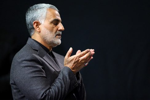 عکس با کیفیت تصویر شهید سردار قاسم سلیمانی سردار شهید در حال دعا کردن با کت شلوار طوسی و پس زمینه مشکی