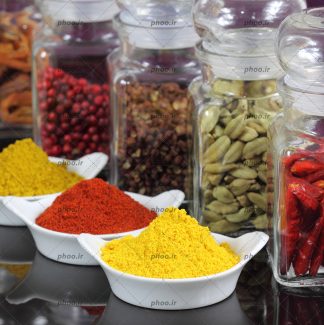 عکس ادویه ها و گیاهان متفاوت در ظرف های شیشه ای و کاسه های سفید در پس زمینه مشکی