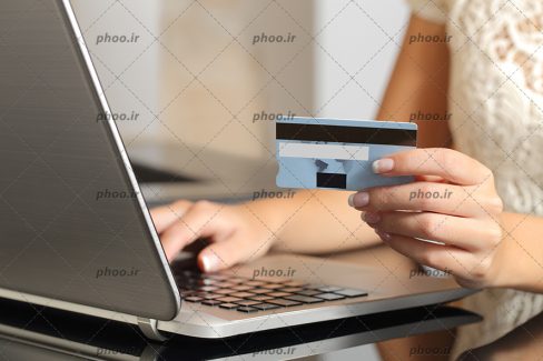عکس کارت عابر بانک در دست زن جلوی لپ تاپ نقره ای نشسته