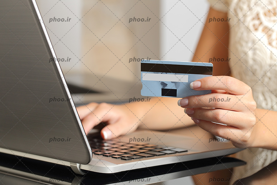 عکس کارت عابر بانک در دست زن جلوی لپ تاپ نقره ای نشسته