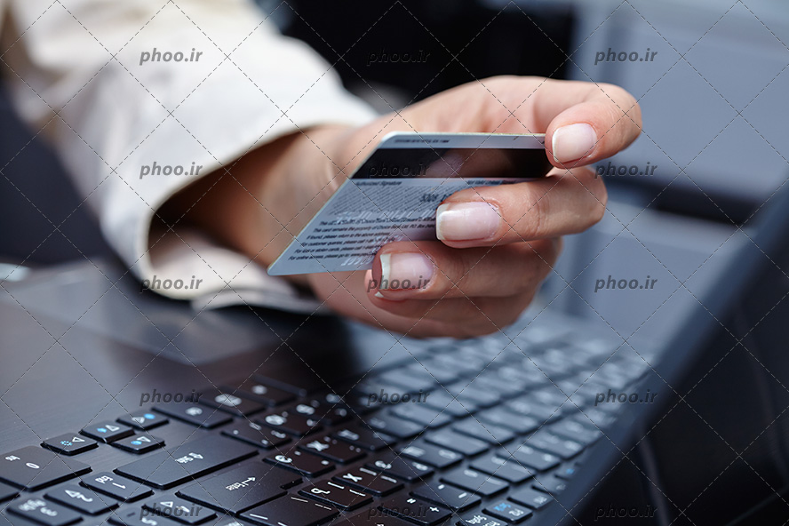 عکس کارت عابر بانک در دست و لپ تاپ نقره ای