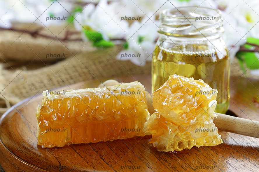 عکس شیشه عسل و قاشق روی تخته چوبی