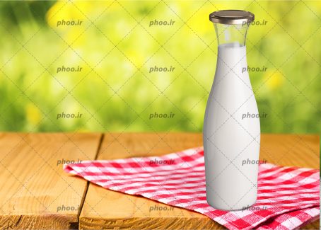 عکس بطری شیشه ای شیر روی میز در پس زمینه محو سبز