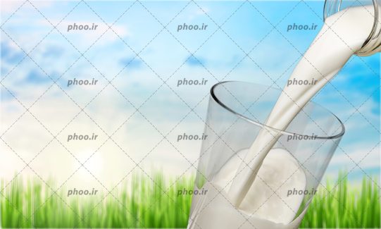 عکس ریختن شیر از بطری شیشه ای در لیوان در پس زمینه چمن سبز و آسمان آبی