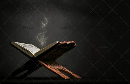 عکس با کیفیت قرآن بر روی رحل چوبی و نور زرد بیرون آمده از آن در زمینه مشکی