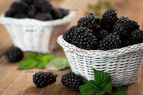 عکس تمشک های سیاه داخل سبد ها و روی زمین در پس زمینه چوبی