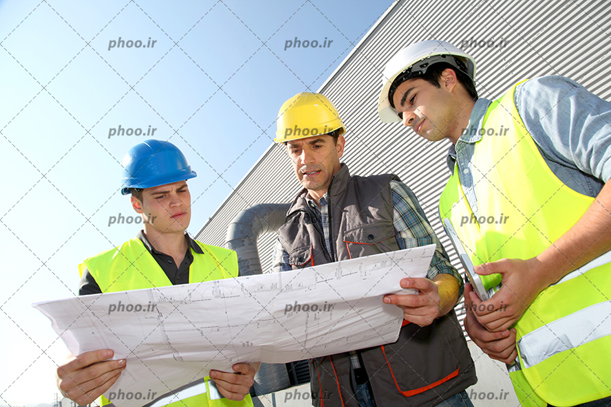 عکس یک معمار و دو کارگر در حال بررسی نقشه ساختمان