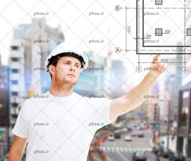 عکس مهندس با کلاه ایمنی و تیشرت سفید در حال اشاره به نقشه