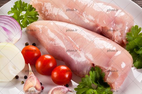 عکس فیله مرغ در کنار پیاز و گوجه و سیر در پس زمینه سفید