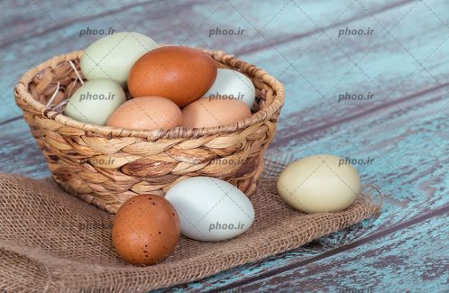 عکس تخم مرغ های داخل سبد و روی زمین در پس زمینه چوبی