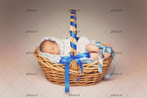 عکس با کیفیت نوزاد تازه متولد شده خوابیده در سبد تزئین شده با روبان آبی